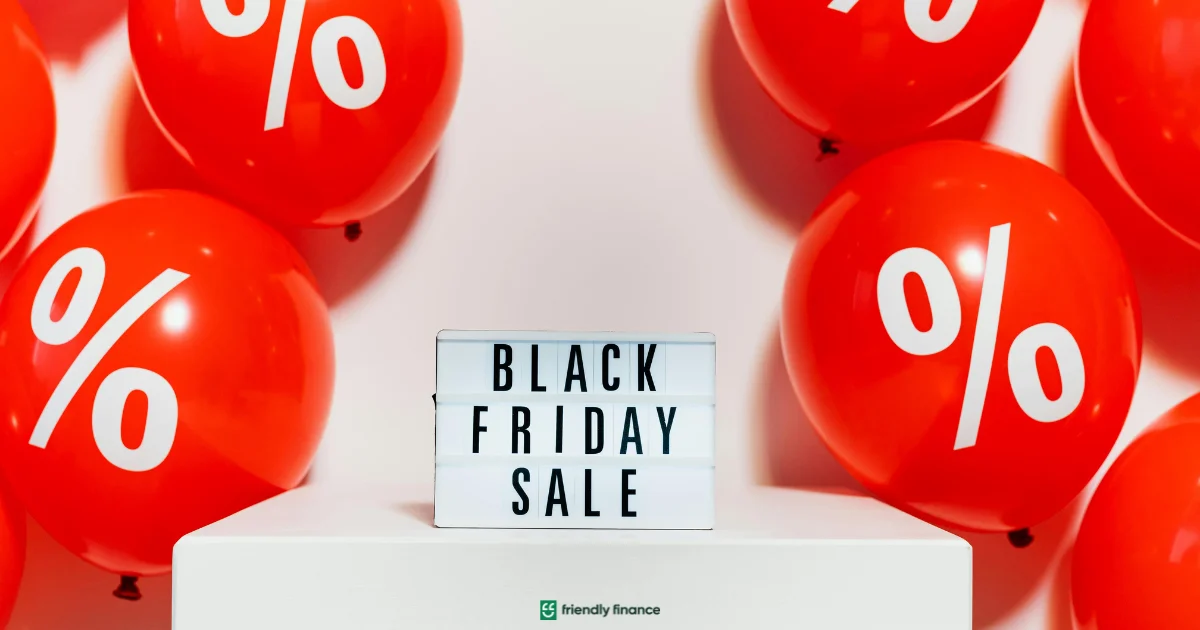 A white lightbox sign reading 'BLACK FRIDAY SALE' surrounded by bright red balloons printed with white percentage symbols.