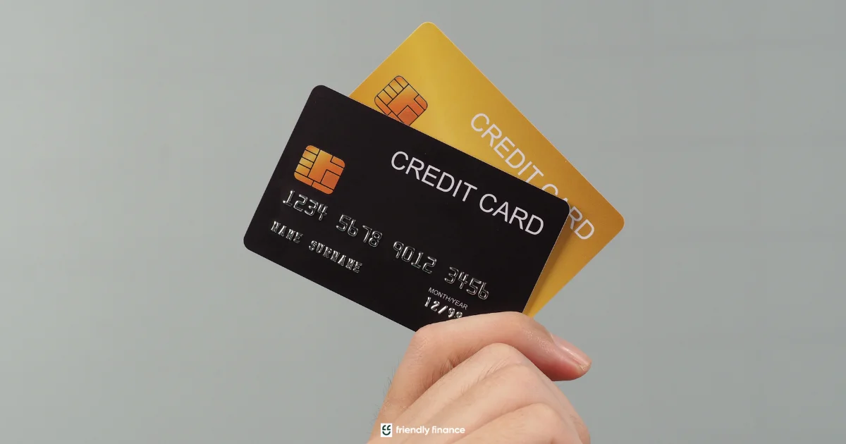 A hand holds up two credit cards, one black and one gold, against a plain grey background.