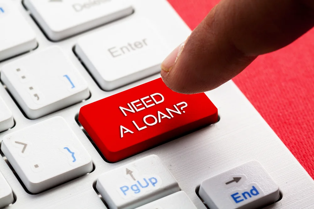Finger pressing a red keyboard key labeled “Need a loan?”