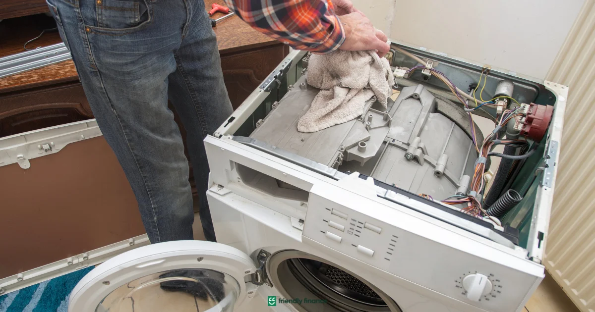 A person repairing a washing machine, wiping the internal drum components with a cloth while the appliance is disassembled.