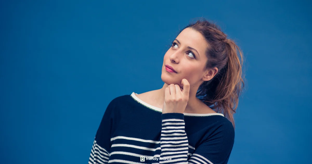 A young woman stands against a blue background, looking up thoughtfully with her hand on her chin, as if considering a financial decision.